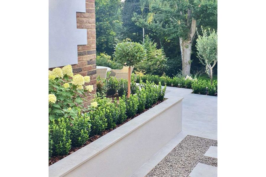 Steel Grey Porcelain Paving patio terrace, with contrasting gravel at base of raised bed filled with low hedging and hydrangea.