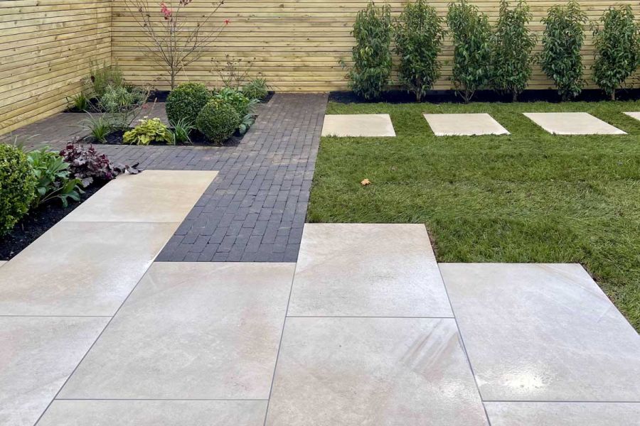 Porcelain patio leading into dark clay pavers and a porcelain stepping stone path cutting through a lawn.