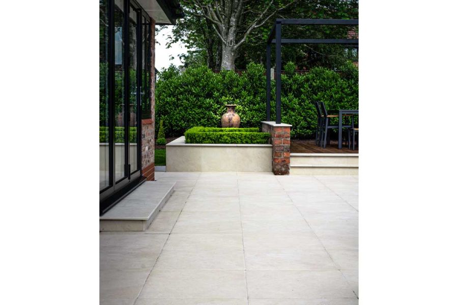 Patio of Slab Khaki Porcelain Paving Slabs laid stack bond, with chamfer step up to glass doors of house. Design by Robert Hughes.