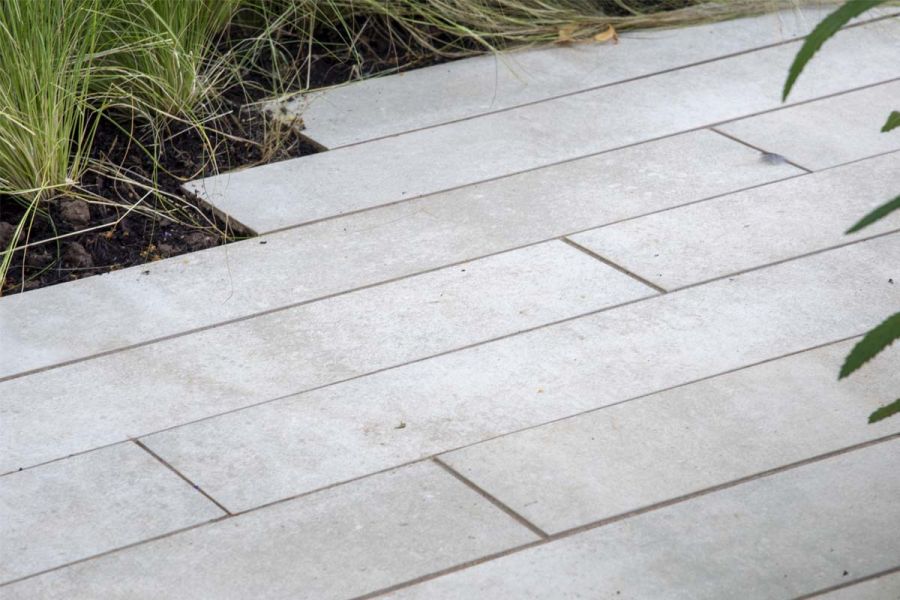 Close up picture of Cream porcelain planks laid in a stretcher bond pattern with ornamental grasses from a nearby bed spilling onto the paving.