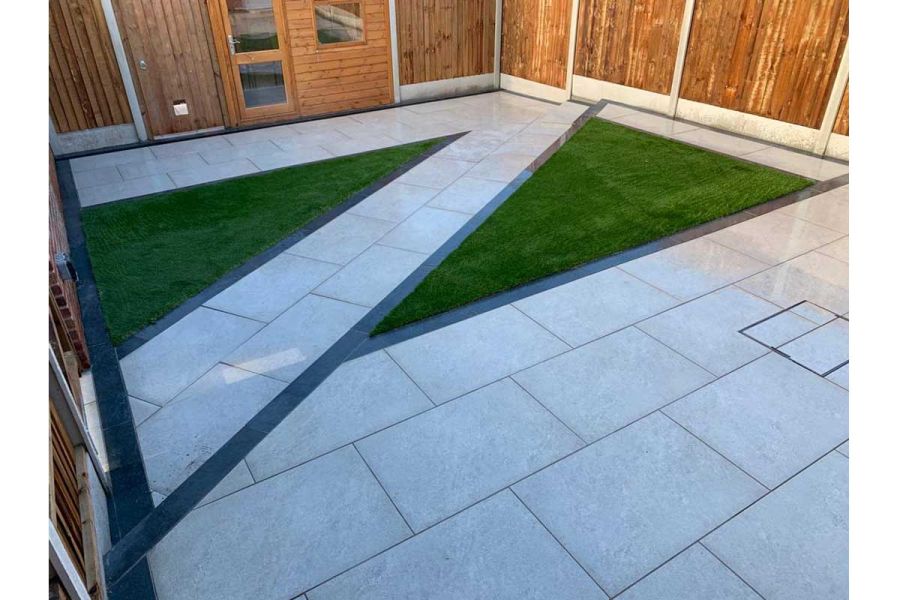 Fenced back garden. Path cuts artificial lawn diagonally, connecting paving on either side edged with Charcoal porcelain planks.