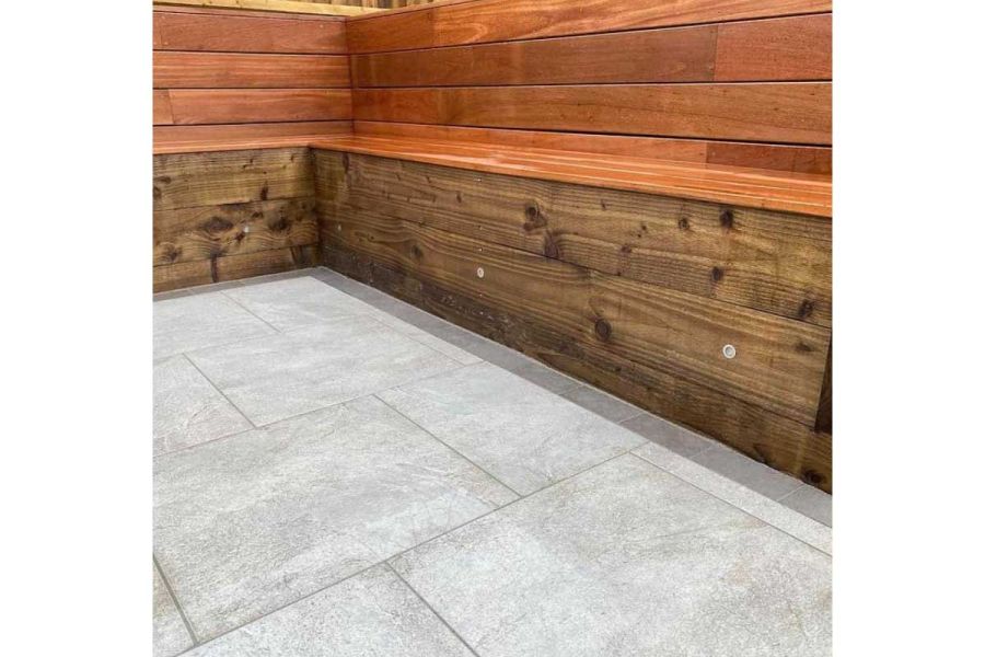 L-shaped wooden bench seat next to grey paving with Steel Grey porcelain sett outline. Built by GRC Landscapes.