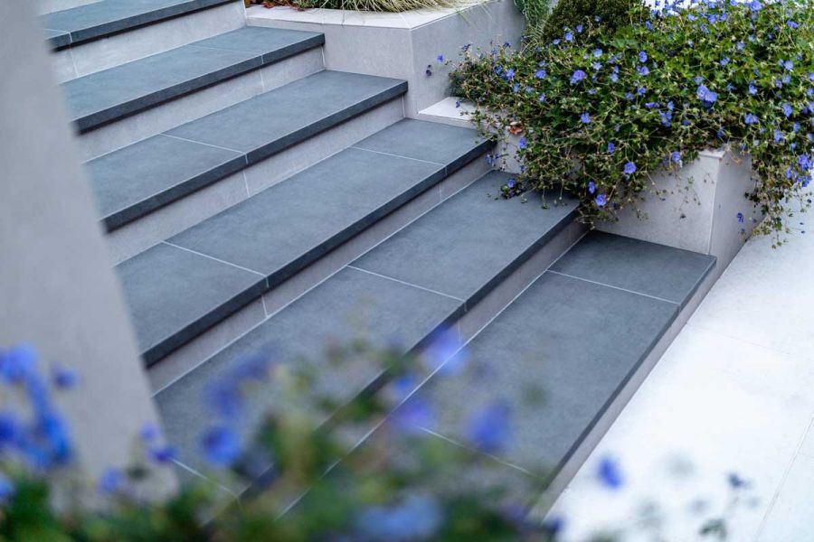 Steel Grey porcelain steps with 20mm downstand, next to DesignClad-faced stepped planters. Design by Gardens of the Future. 