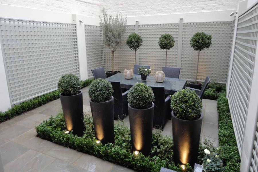4 topiary balls in tall pots in tiny courtyard paved with Kandla Grey sandstone slabs, with dining table and clipped trees.