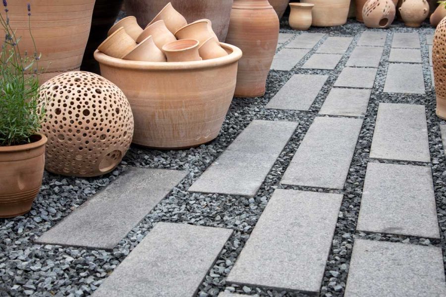 Dark grey granite narrow paving slabs laid in matching gravel, surrounded by terracotta pots of different shapes and sizes.