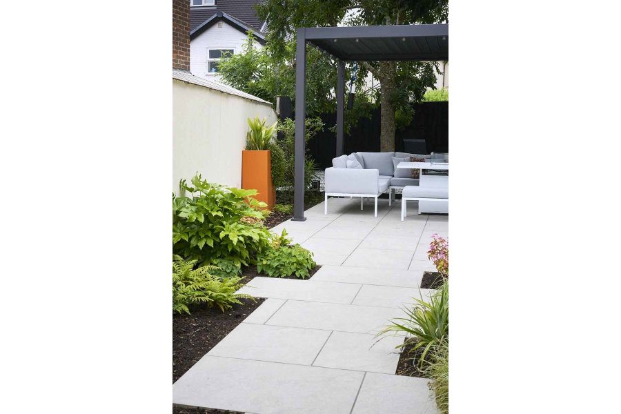 half-view of proteus grey aluminium pergola with furniture underneath, astor grey porcelain leads up with planting either side.