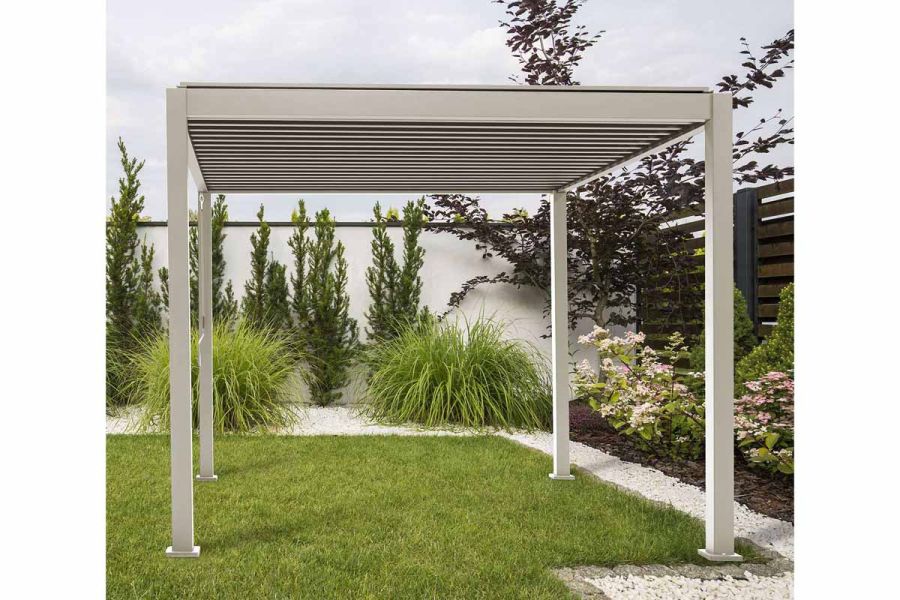 Proteus White Aluminium Pergola stands on grass, flowerbeds behind. Slim powder-coated aluminium legs support louvred flat roof.