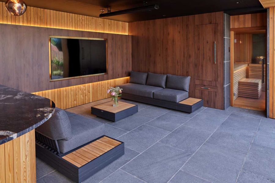TV screen set in wall between 2 3-seater sofas in interior paved with Black granite paving slabs with pale-grouted joints.