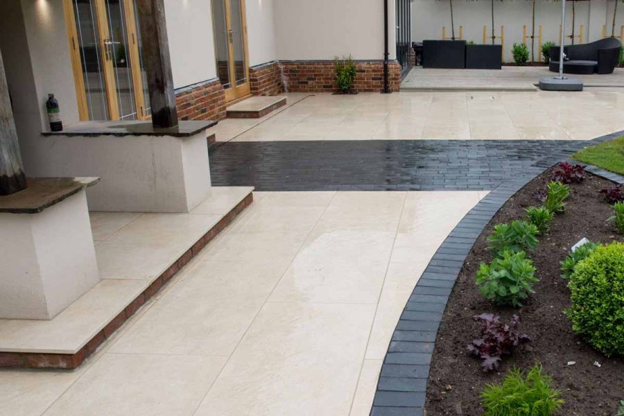 Midnight Black limestone setts edge curved bed and contrast with cream paving of patio with porch over back door.
