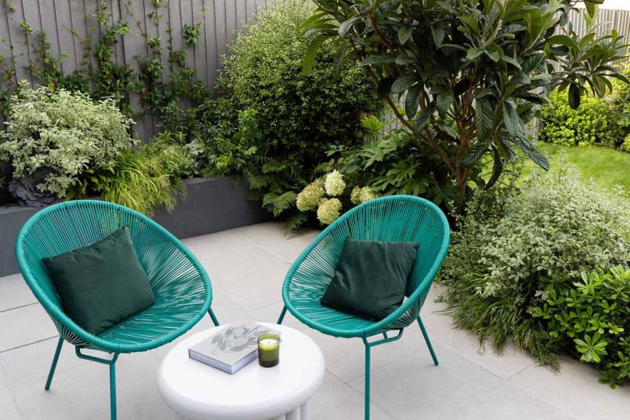 2 aqua green wire chairs sit around unique side table, on topof florence grey porcelain paving, surrounded by greenery.