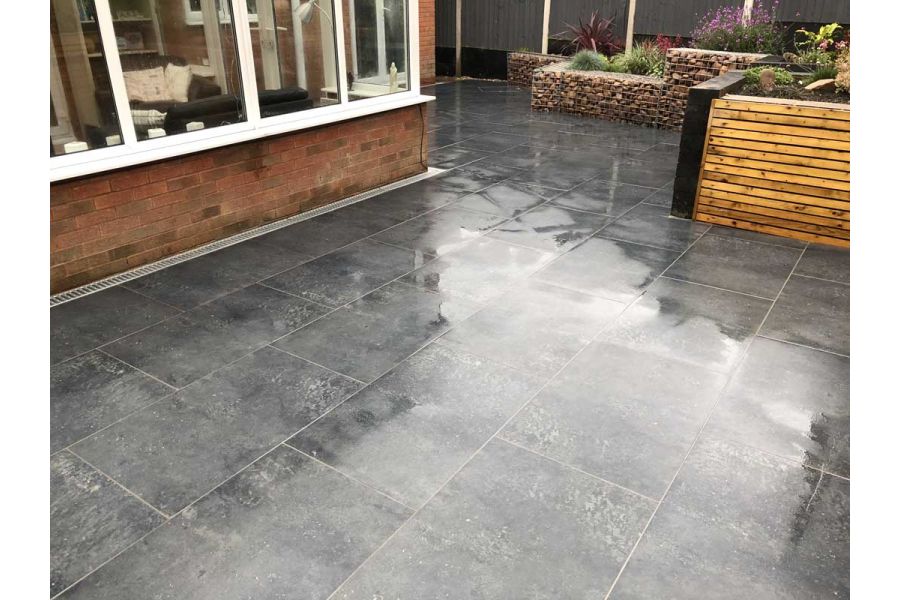 Charcoal porcelain paved patio outside a conservatory surrounded on one side by raised beds made from timber and gabion cages.