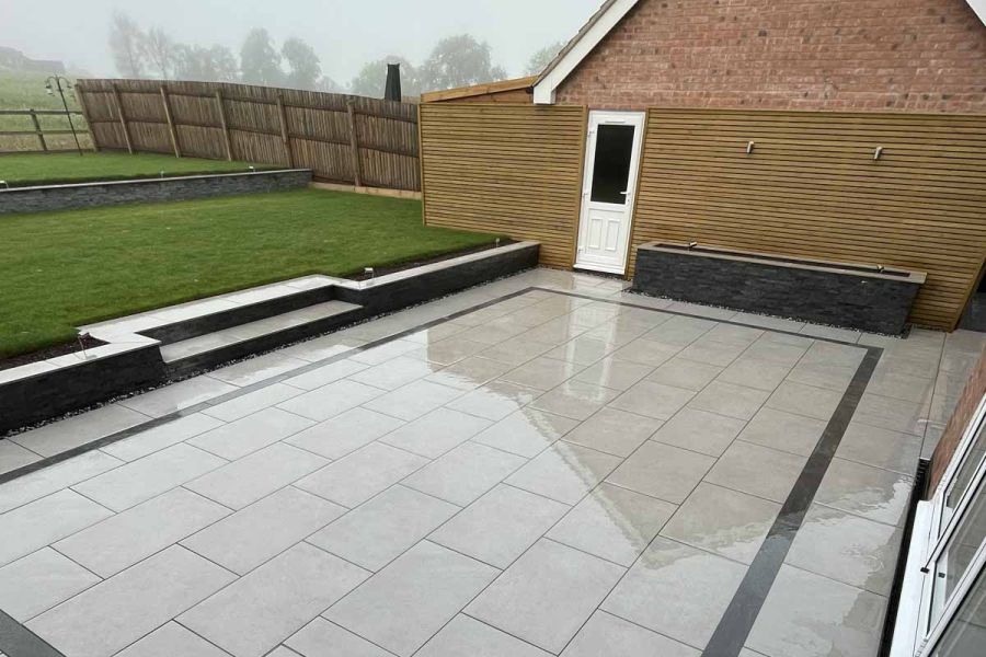 2 steps up to lawn from wet oblong grey patio with decorative inset frame of Platinum Grey porcelain planks. Design by Ravenstone.