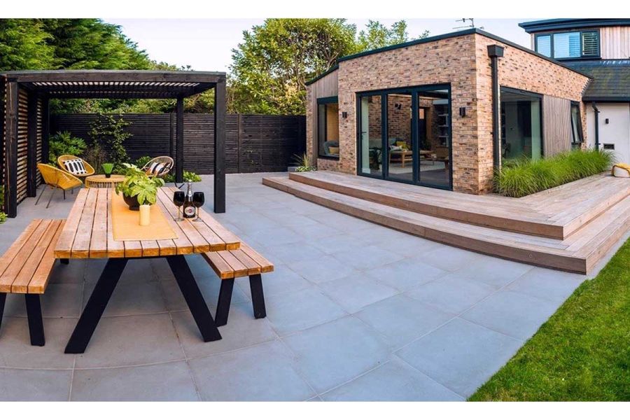 Modern brick building with wide wooden steps down to patio of Cement porcelain paving.  built by Brockstone Landscape Construction.