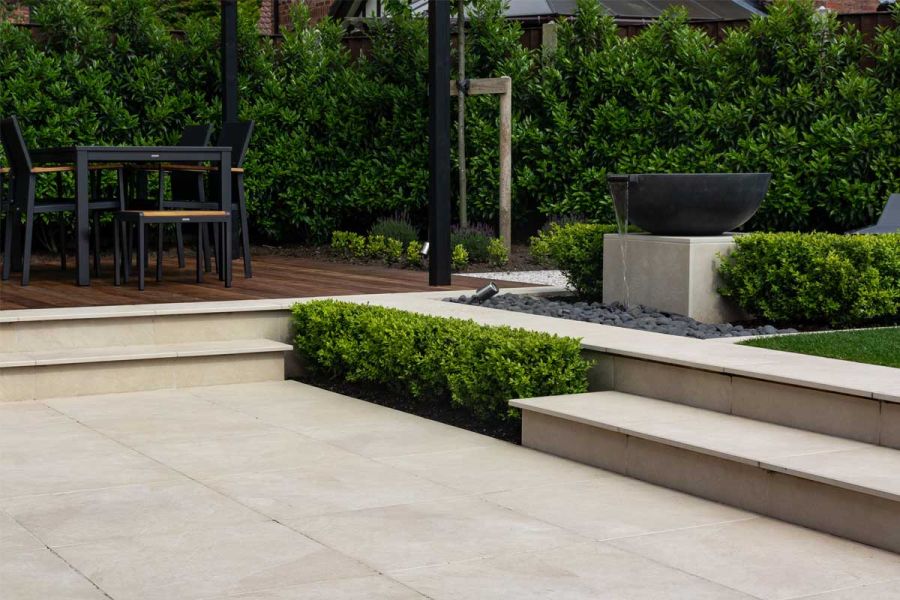 2 Slab Khaki Porcelain outdoor steps rise to dining area and turn 90°to access lawned area. Lower step interrupted by low hedge.