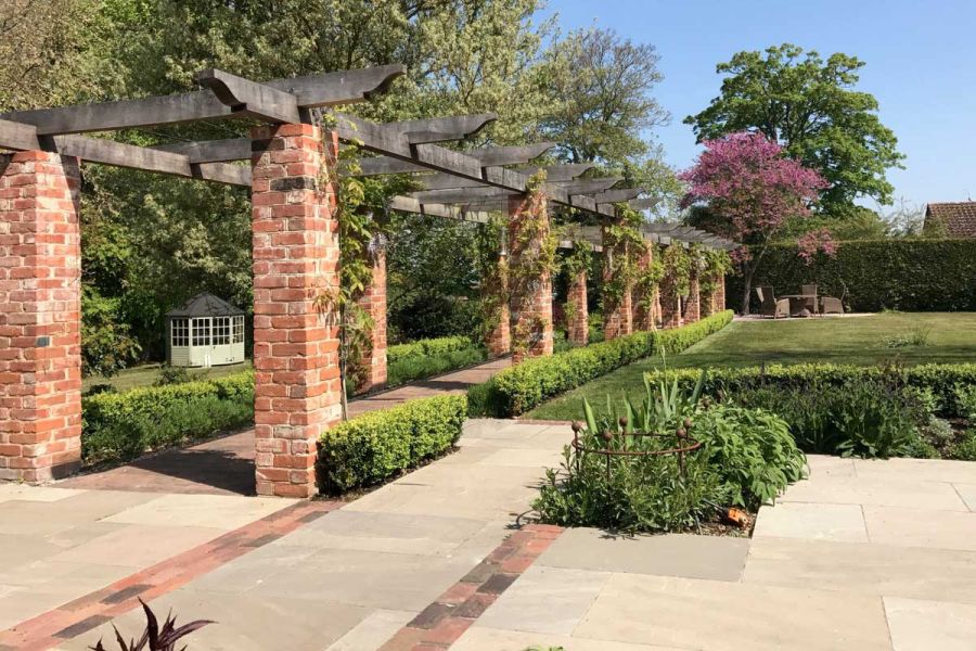 Large garden with low hedging and lawn, long colonnade of brick pillars, and paving detailed with Romsey Antique Belgian Bricks.