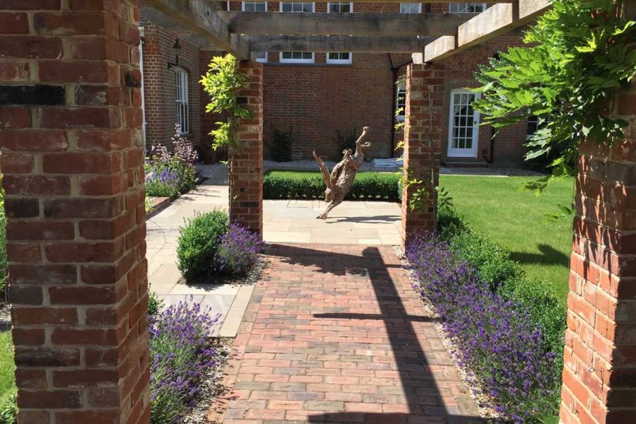 Romsey Antique Clay pavers, under brick-pillared, lavender-lined colonnade, lead to giant hare sculpture on natural stone flags.