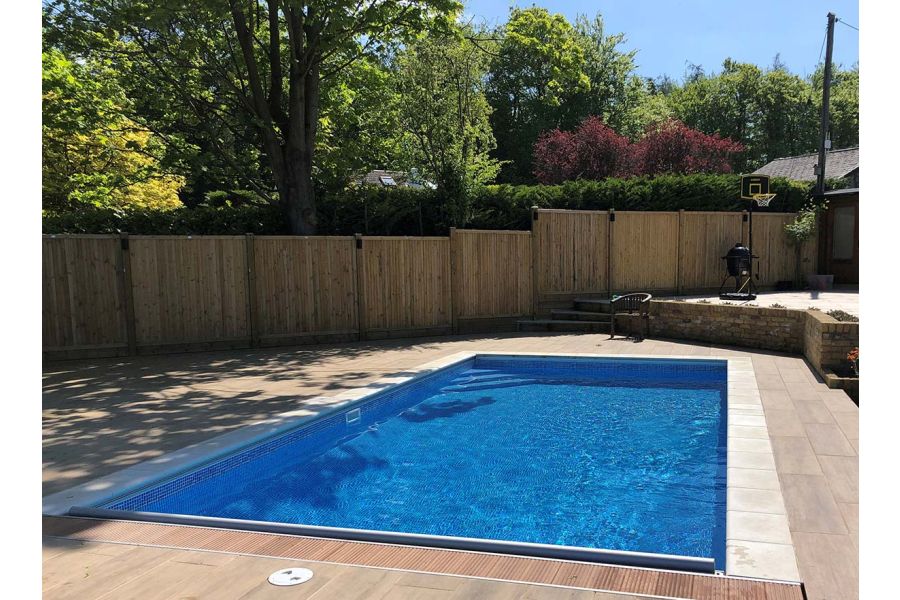 Swimming pool in a back garden with Rovere wood effect porcelain paving surround and closed board fencing panel boundary.