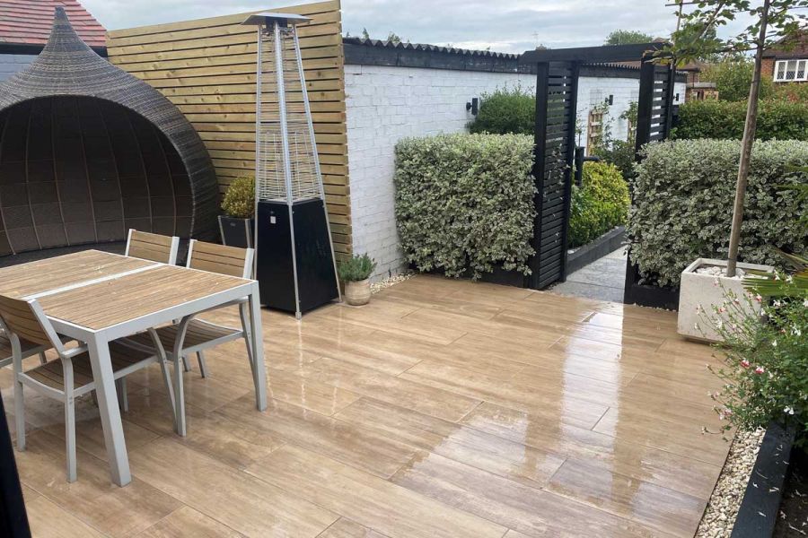 Garden furniture, egg chair and patio heater sits on wet rovere porcelain paving patio, pathed area leads to other part of garden.