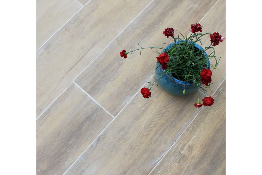 Blue plant pot planted with red flowers sitting on top of Rovere wood effect porcelain outdoor tiles grouted with a light grey grout.