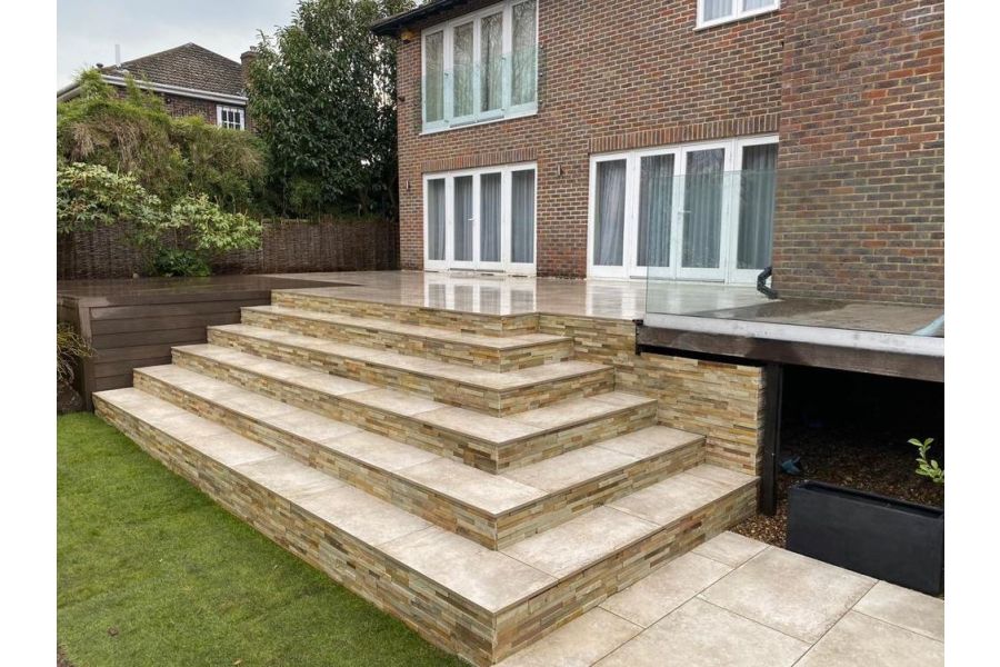 6 deep steps in Frosty Grey Porcelain with stone-clad risers ascend from lawn to matching patio with 2 sets of doors from house.