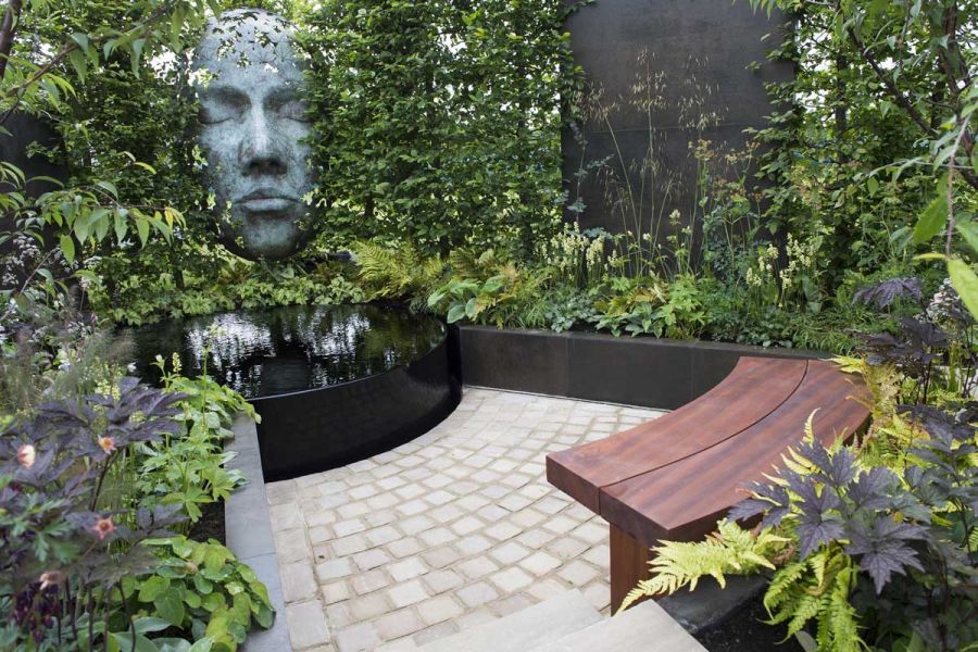 Raj Green cobble setts form deep arc between black raised bed with lush planting and curved wooden bench. Design by Richard Rogers.