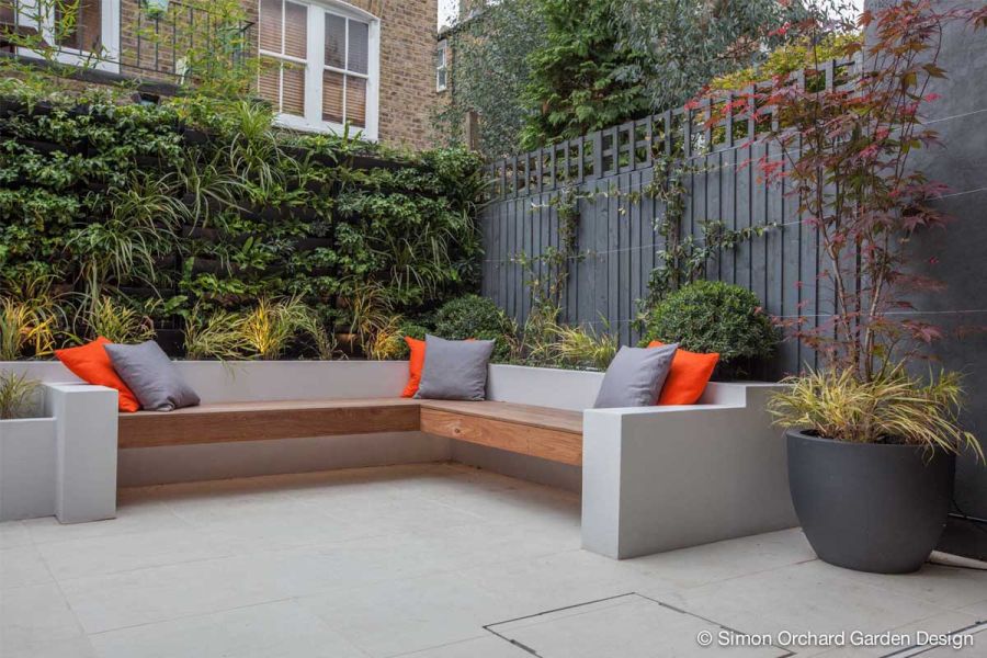 Plant wall and grey fence behind white raised beds with bench attached and Sandy White Porcelain paving. By Simon Orchard Gardens.