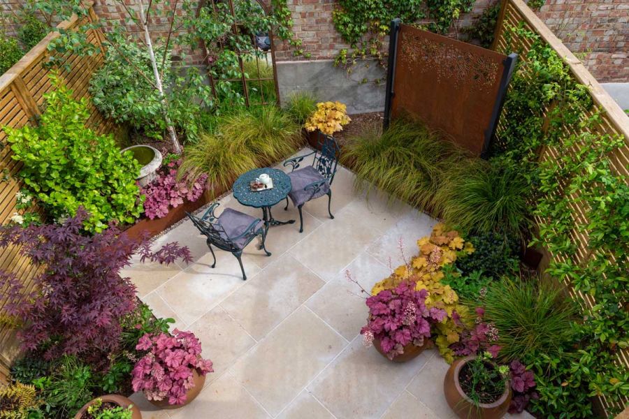 Small fenced and walled garden paved with Jura beige limestone patio set at 45 degrees to create angular beds. Design by Sarah Kay.