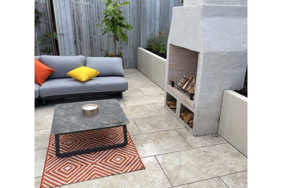 Table on mat between sofa and outdoor fireplace set into raised bed with desert beige exterior cladding. Design by Scott Taylor.