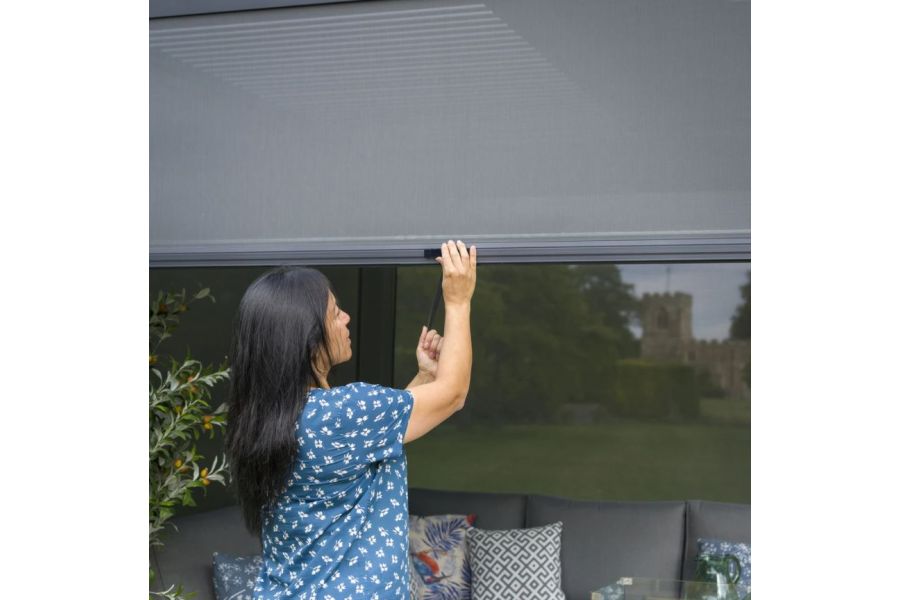 Woman adjusting the side screen of a Dark Grey Metal Pergola, one hand holding pulling loop, the other on a catch.