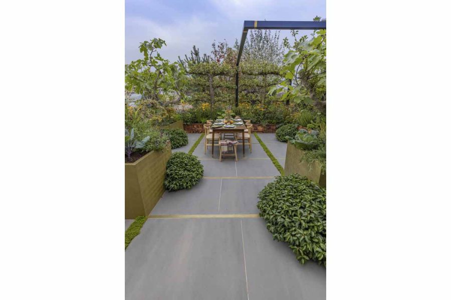 Porcelain pathway into a country styled garden with large corten steel effect planters leading towards a garden table and chairs.