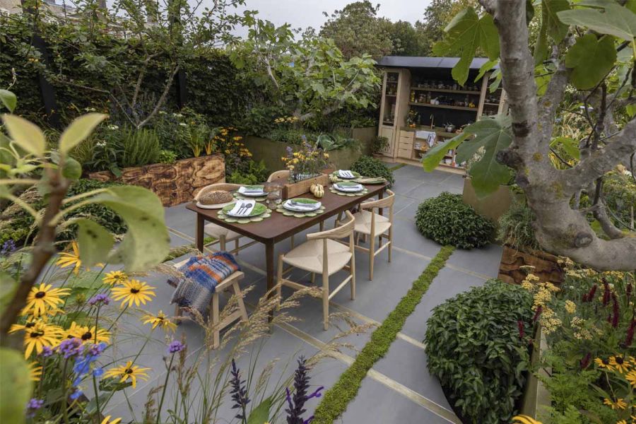 Laid outdoor dining table in a heavily planted garden with a Sidewalk porcelain patio.