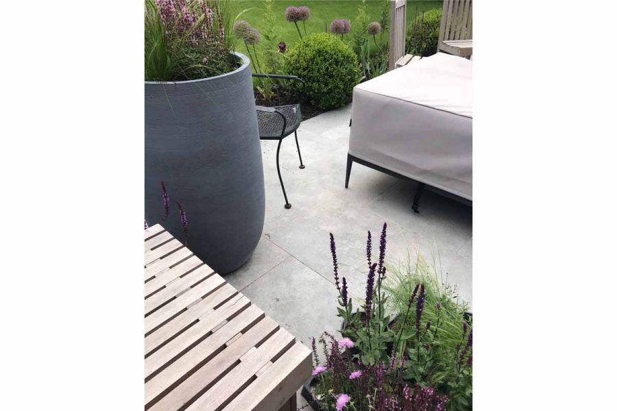 Garden furniture and two planters with purple-coloured planting sit on a Silver Contro Porcelain patio by Greencube Landscapes.