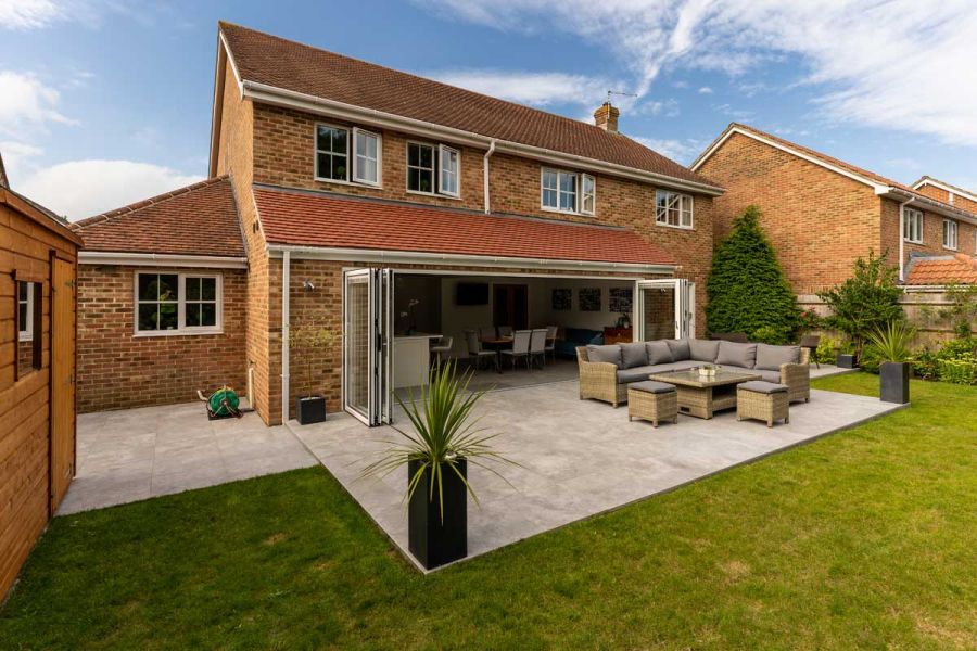 Large rectilinear patio in Silver Contro Porcelain slabs, with modular garden furniture, at rear of house with open bifold doors.