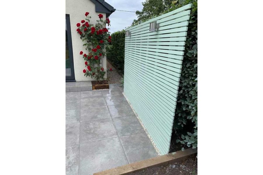 Silver-Contro Porcelain paving by eau-de-nil battened panel. Red roses growing next to paved step. Designed by Oakley Landscapes.