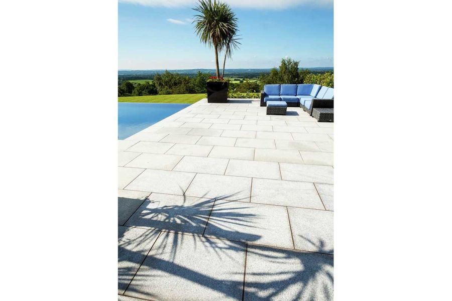 Pool-side terrace of Silver Grey granite paving slabs, with L-shaped sofa, potted palm, and sunny view to distant horizon.