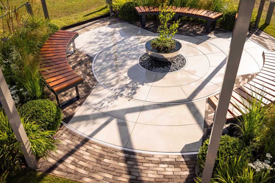 Segment of paving circle. Silver Grey Multi brick pavers form edging  and sit under curved slatted wood bench. Built by Mustard Seed.
