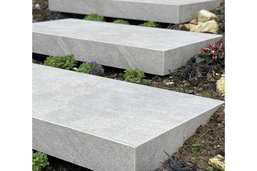 Close view of 3 bespoke Silver Grey porcelain steps with downstand at side and front, set into soil with creeping plants.