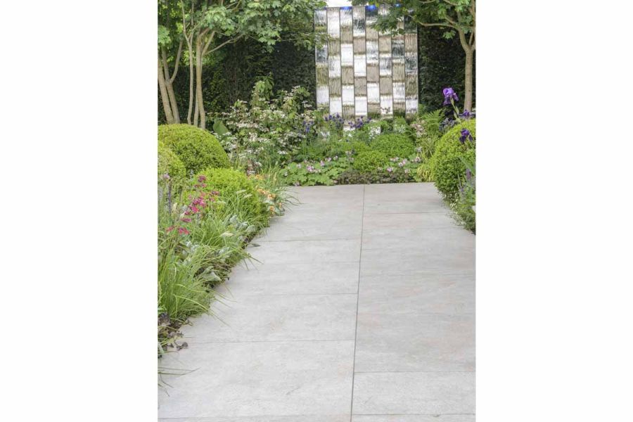 Silver-grey porcelain paving between dense planting, by Nic Howard Designs for RHS Chelsea 2016. Woven silver sculpture beyond.
