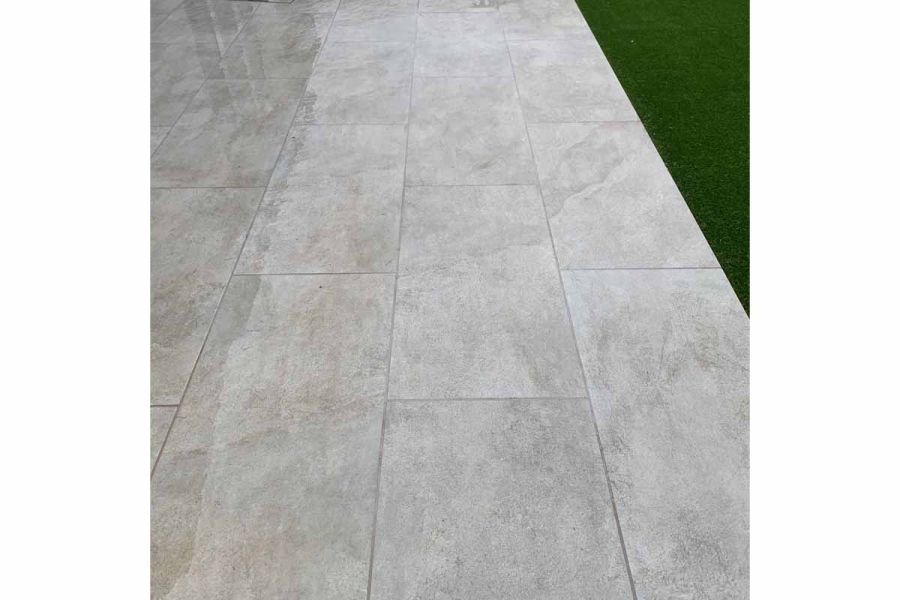 Close up shot of Silver Grey Porcelain paving in the wet, showing its colour and texture. patio tiles have been jointed with grey mortar.