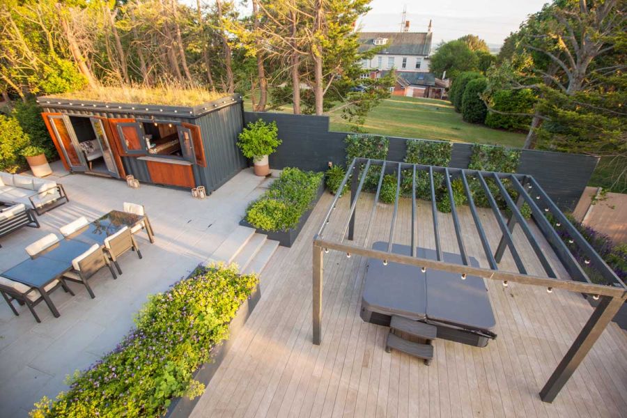 Paved garden with hot tub under pergola on Cinnamon composite decking boards and steps up to dining area. Design by Simon Orchard.