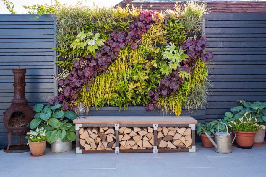 Log storage bench beneath living wall with planted pots on 900x600 Florence Grey porcelain paving. Design by Simon Orchard. 