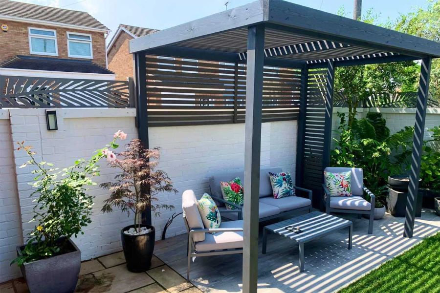 Garden corner with 4-seat grey lounge set under pergola of Pebble Grey Composite Battens. Built by Skyline Fencing and Landscaping.