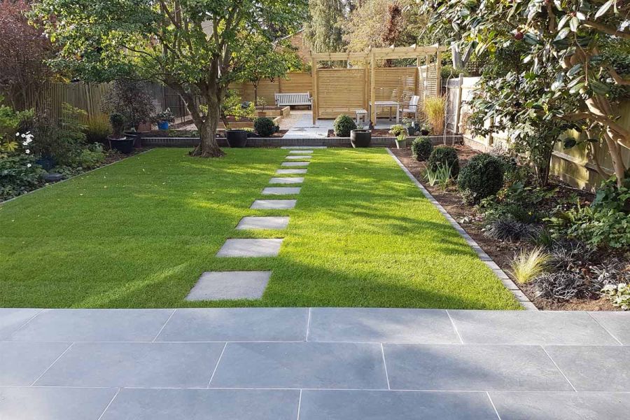 Square stepping stones cross lawn from Slab Coke Porcelain patio to seating area at rear of garden in design by Landscape Artisan.