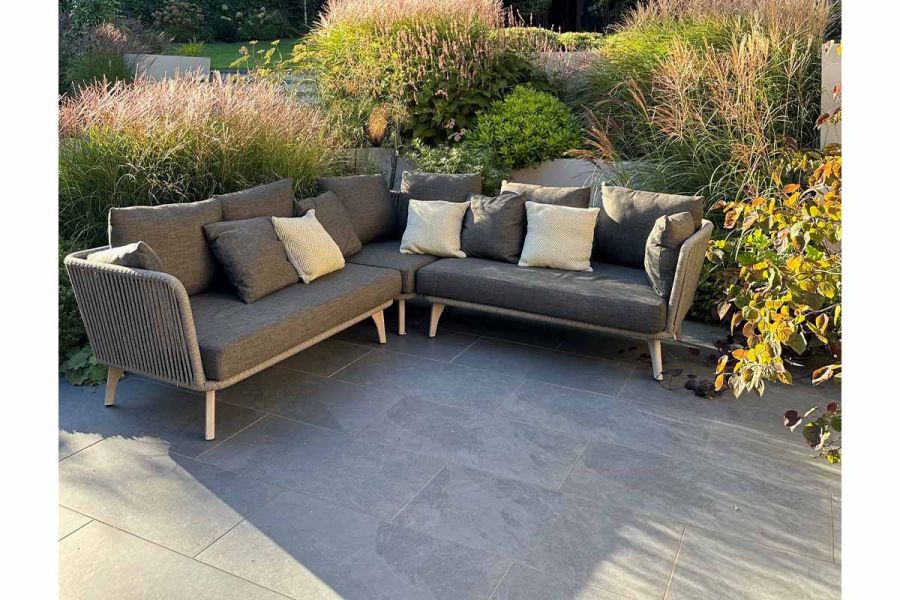 Slab Coke Porcelain paving showing its texture in the shadows, adorned by lush planting and comfy seating area.