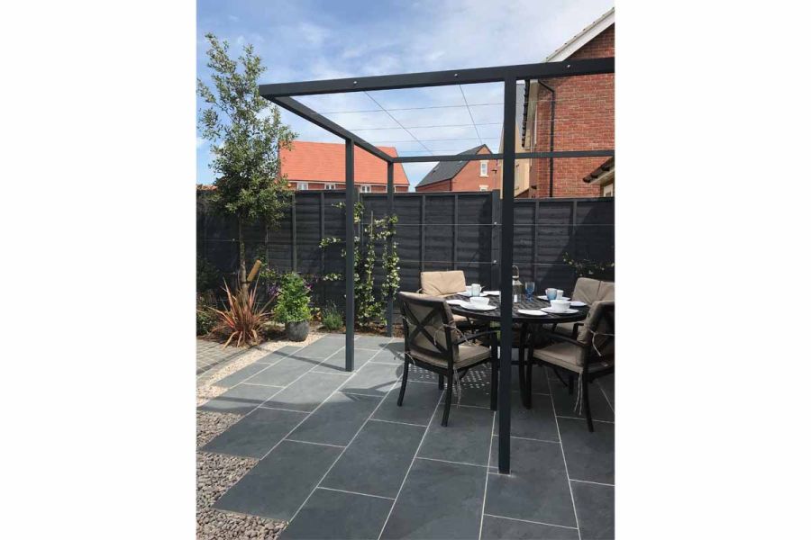 4 chairs and round table under wooden pergola, set into patio of Slab Coke porcelain paving with staggered edges set in gravel.