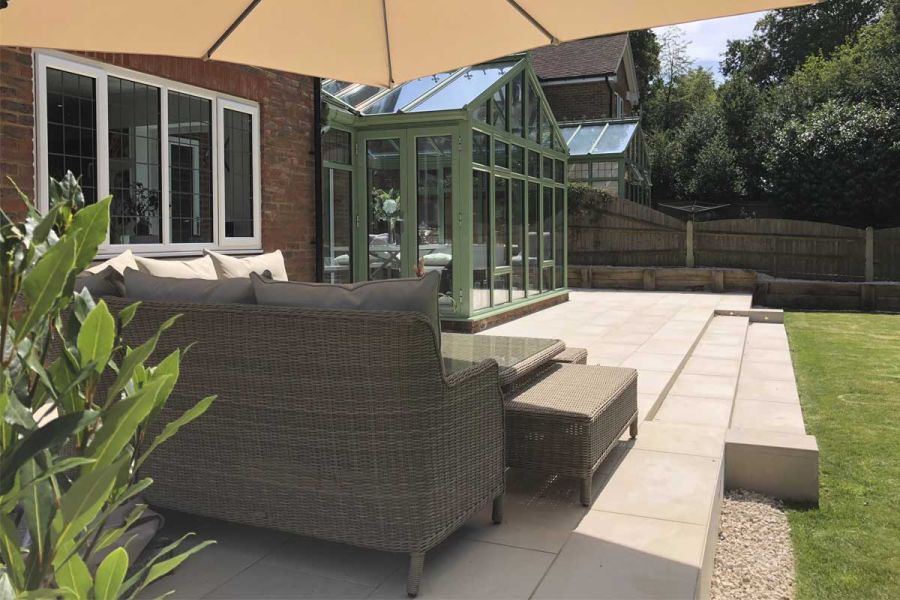 Rattan corner sofa set on Slab Khaki porcelain patio at back of house, with 2 shallow steps down to lawn, built by Aye Gardening.