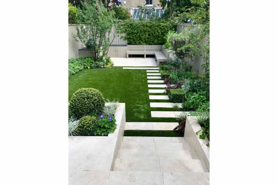 Slab Khaki Porcelain steps descend to path of strips of tiles across lawn to matching paved area with benches at end of garden.