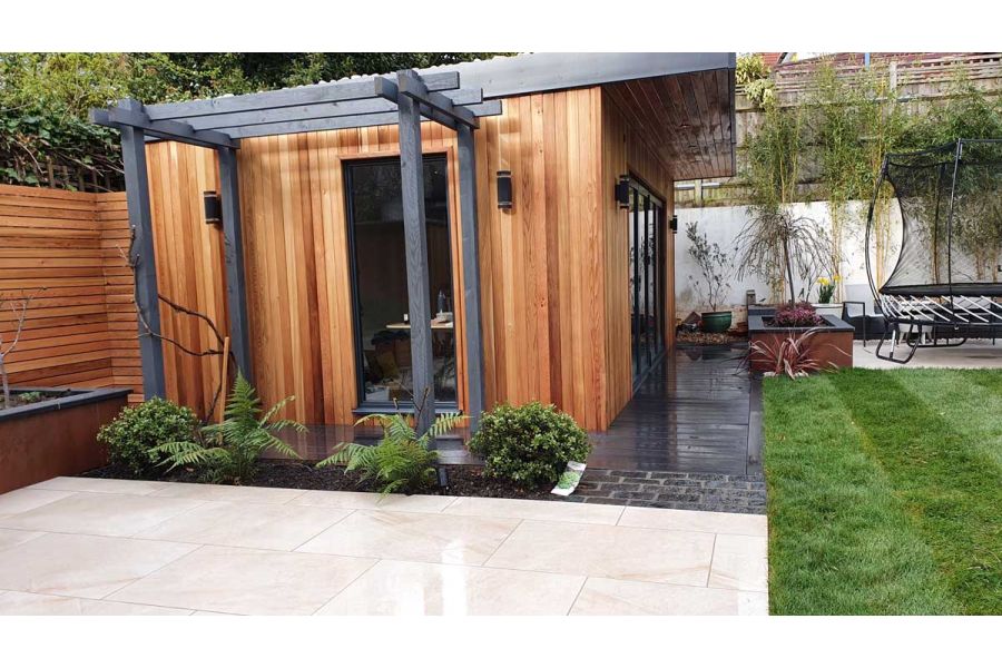 Cedar clad garden office with dark composite decking surround, natural lawn and a porcelain patio.