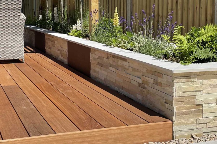 Decking edged with stone-clad wall of raised bed, with panels of Steel Corten Luxury porcelain cladding inserted at intervals.