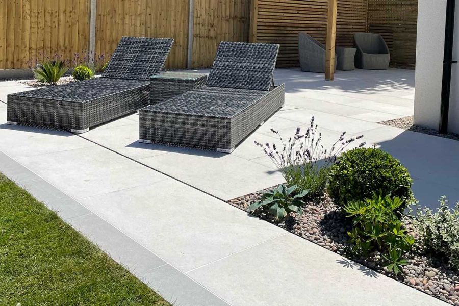 2 rattan sunloungers on Florence White porcelain paving with gravel bed, lawn and slot drain. Design by Smith and Gorman.